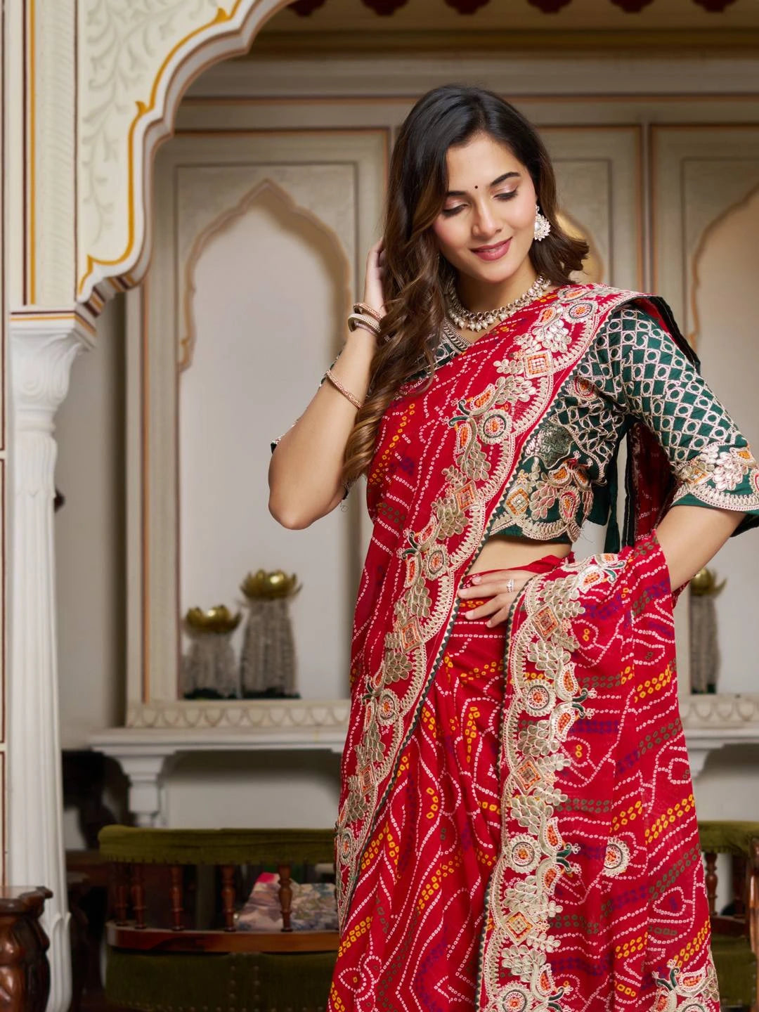 Woman in a red saree with intricate patterns in an ornate room.