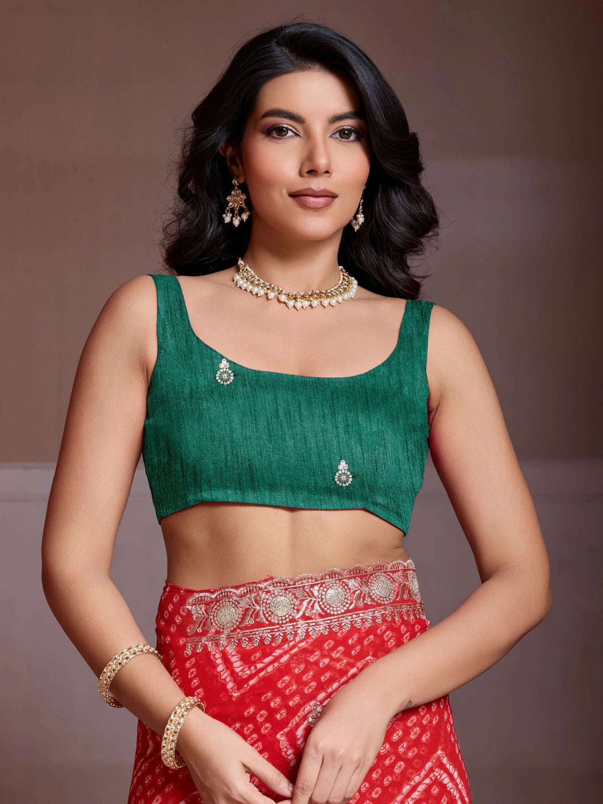 Woman wearing a green blouse and red saree with jewelry against a brown background
