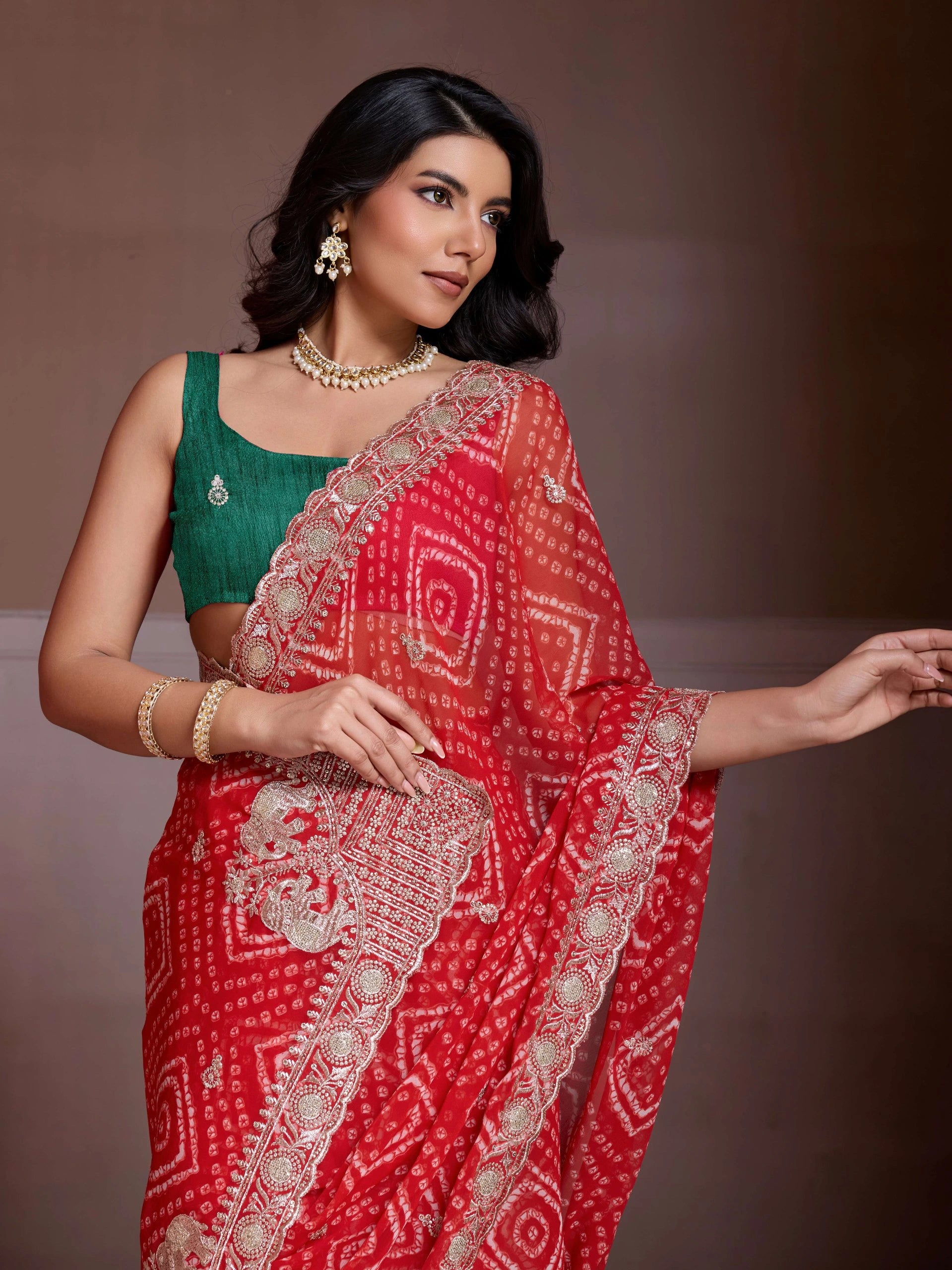 Woman wearing a green blouse and red saree with intricate patterns against a brown background