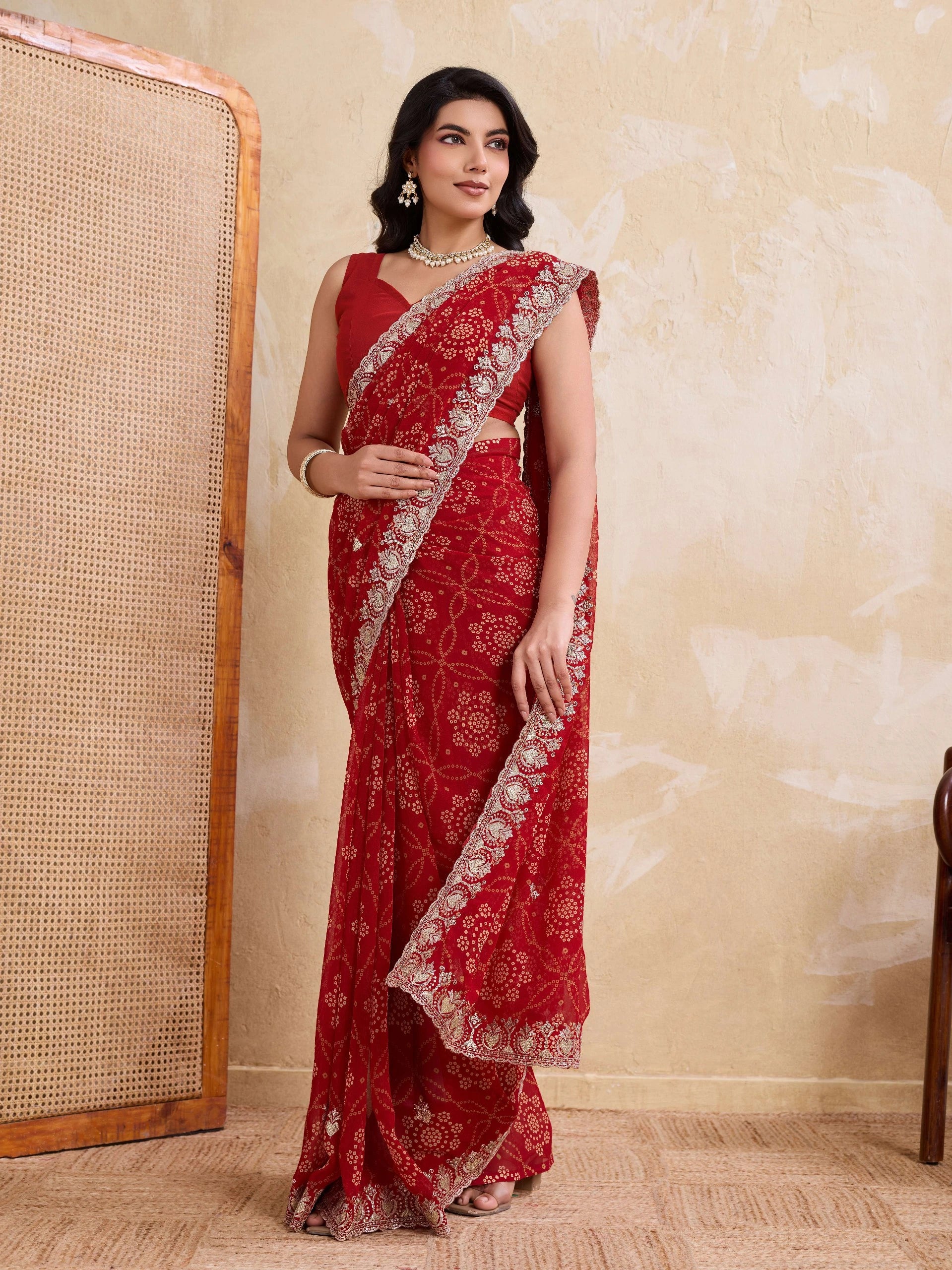 Woman wearing a red saree with white patterns against a beige wall.