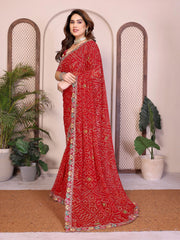 Woman wearing a red saree with intricate patterns in a decorative setting with plants.