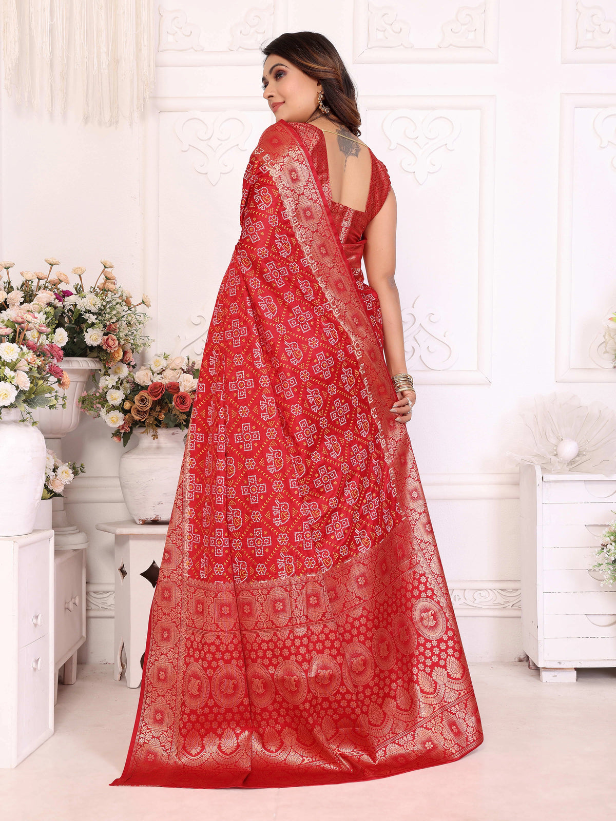 Woman wearing a red saree with white patterns in a decorated room.