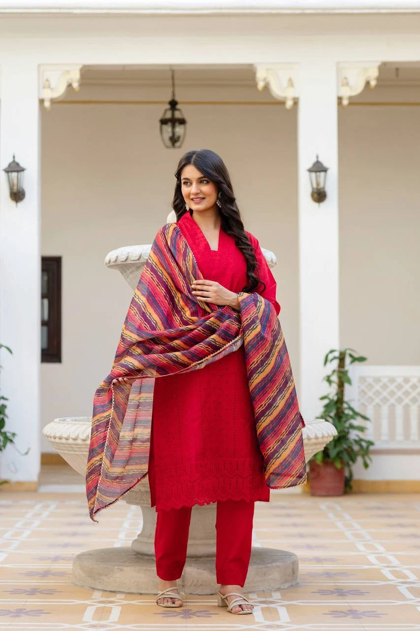 Woman in red traditional outfit with a colorful shawl standing in a decorative indoor setting.