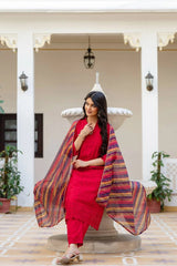 Woman in a red outfit with a colorful shawl standing in an elegant indoor setting.