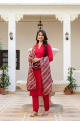Woman in a red outfit with a colorful shawl standing in an outdoor setting.