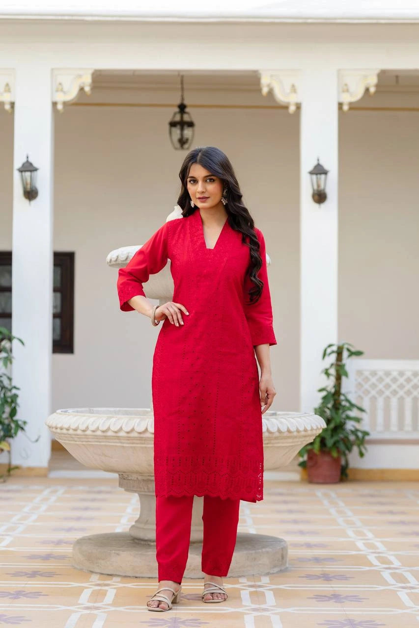 Woman in a red traditional outfit standing in an outdoor setting with white columns and plants.