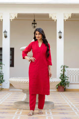Woman in a red traditional outfit standing in an outdoor setting with white columns and plants.
