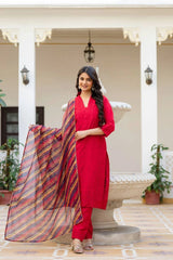 Woman in a red traditional outfit with a colorful scarf standing in an outdoor setting.