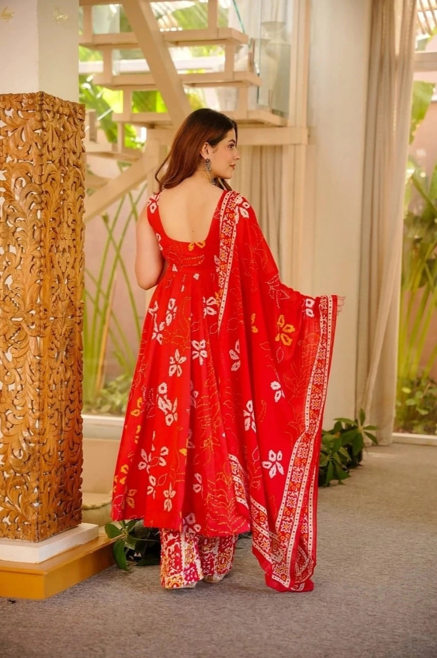 Woman in a red floral dress standing in a decorated room with plants and architectural elements.