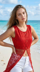 Woman in a red top and white shorts standing on a beach with clear blue water and sky.