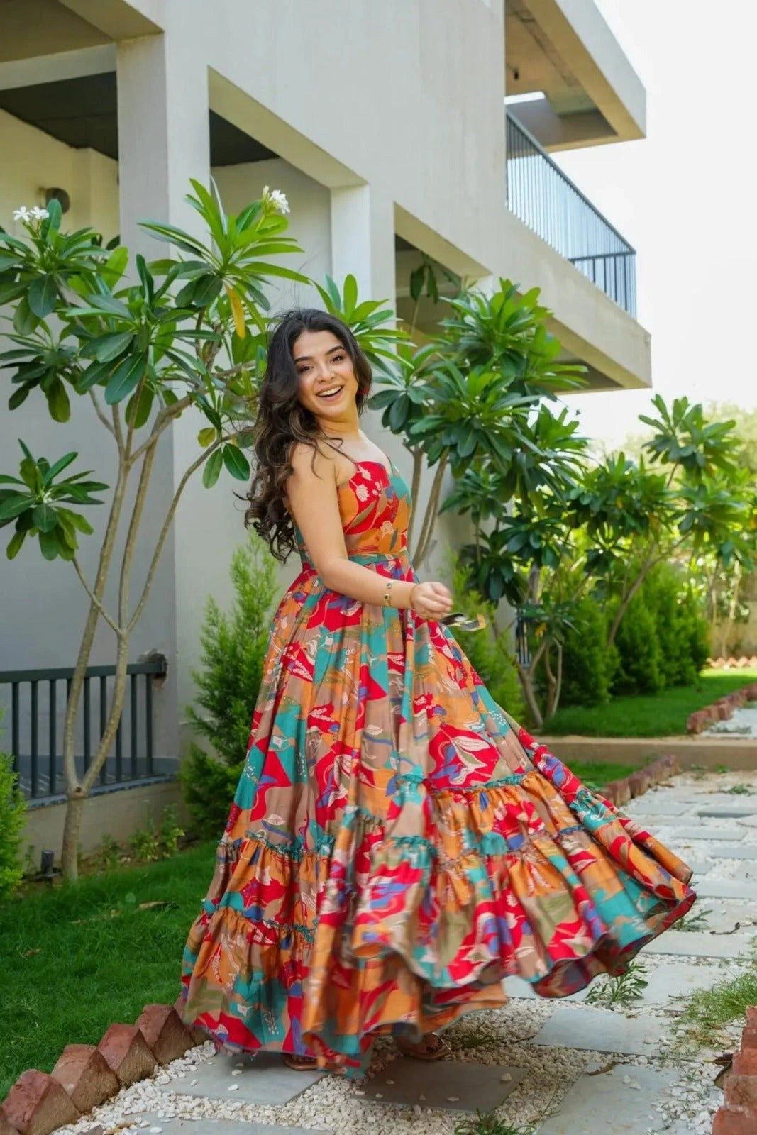 Woman in a colorful dress standing outdoors with greenery and a building in the background