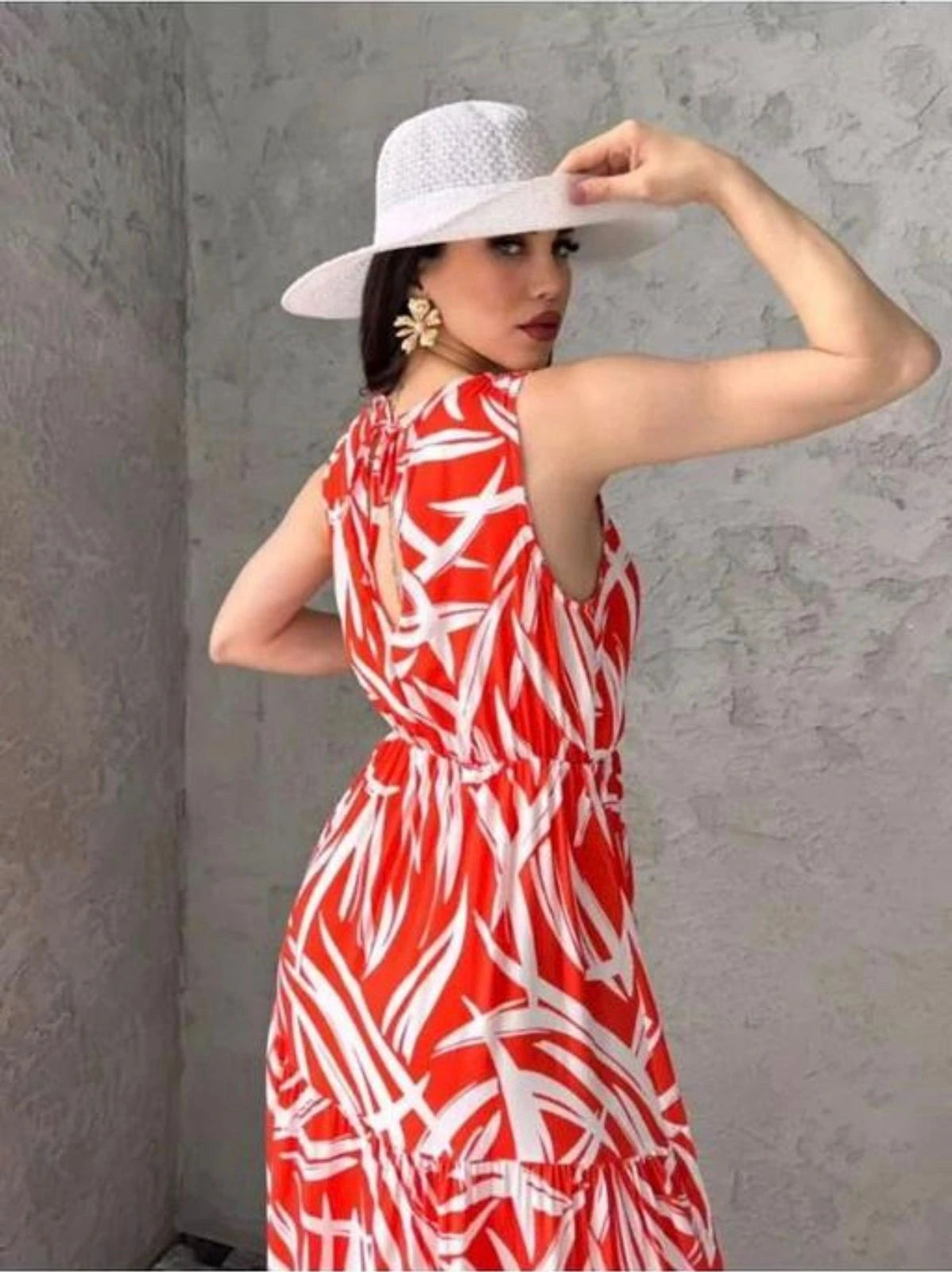Woman wearing a red and white patterned dress with a white hat against a gray wall.