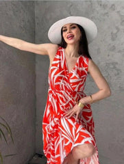 Woman wearing a red and white patterned dress with a white hat against a gray wall.