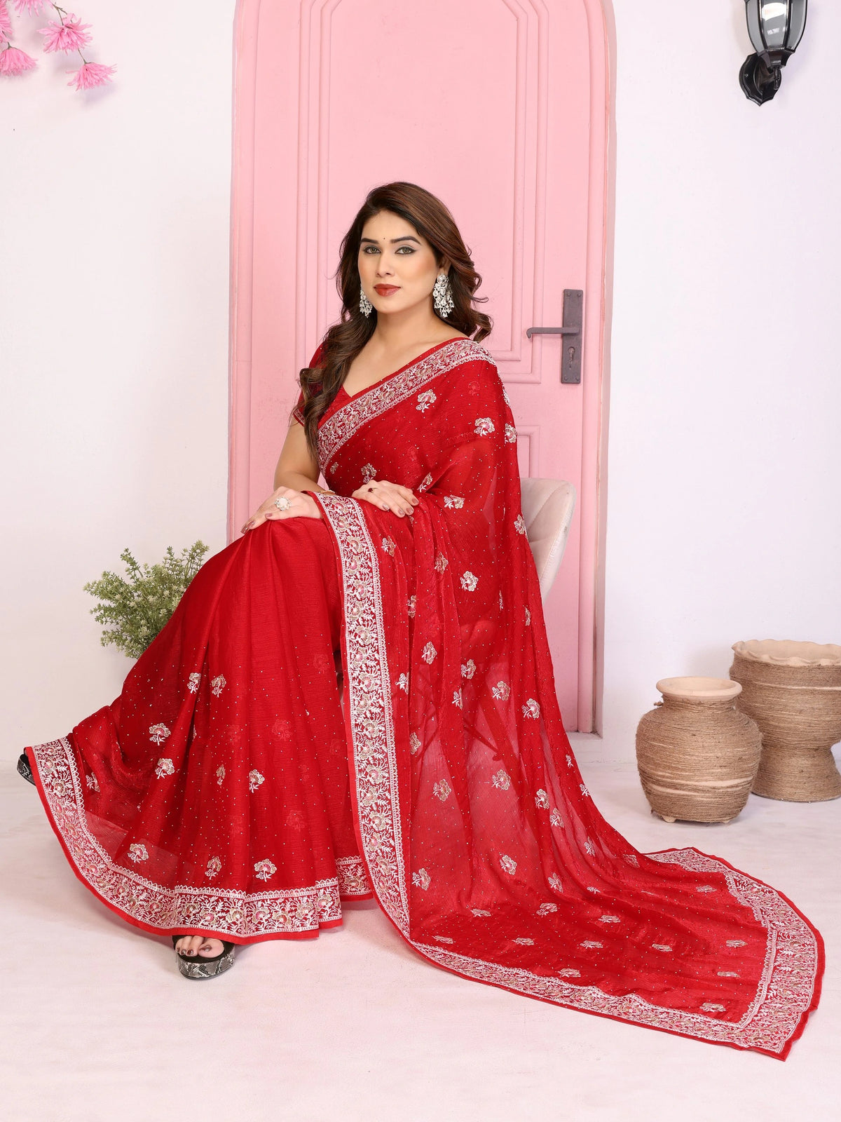 Woman wearing a red saree with white patterns in a minimalistic setting.
