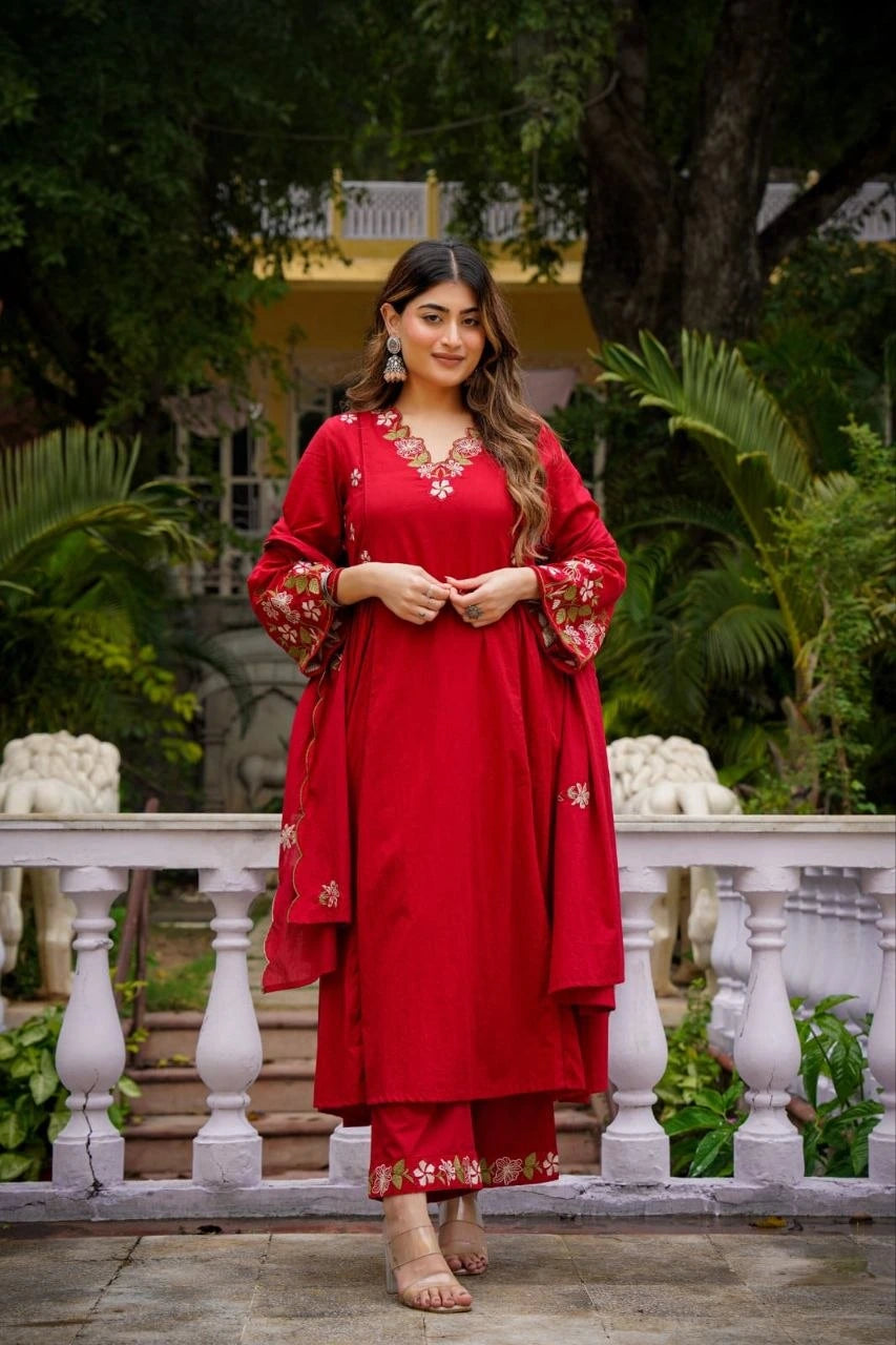Woman in a red traditional outfit standing outdoors with greenery in the background