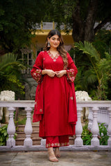 Woman in a red traditional outfit standing outdoors with greenery in the background