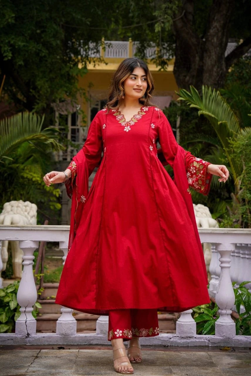 Woman in a red traditional outfit standing outdoors with greenery in the background