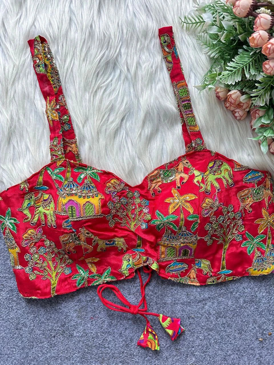 Red embroidered bralette with colorful patterns on a textured surface with flowers.