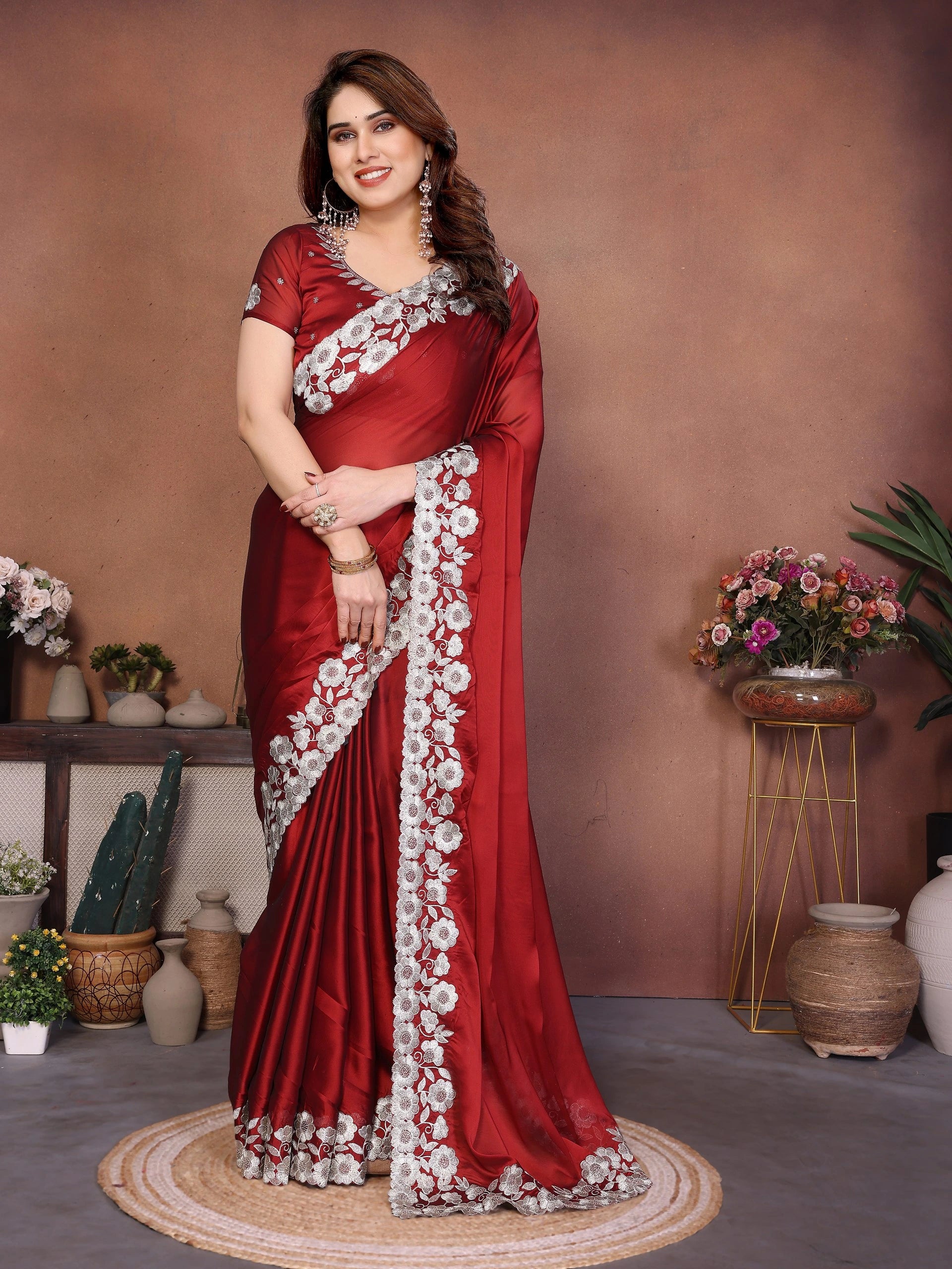Woman in a red saree with white floral patterns standing in a decorated room.
