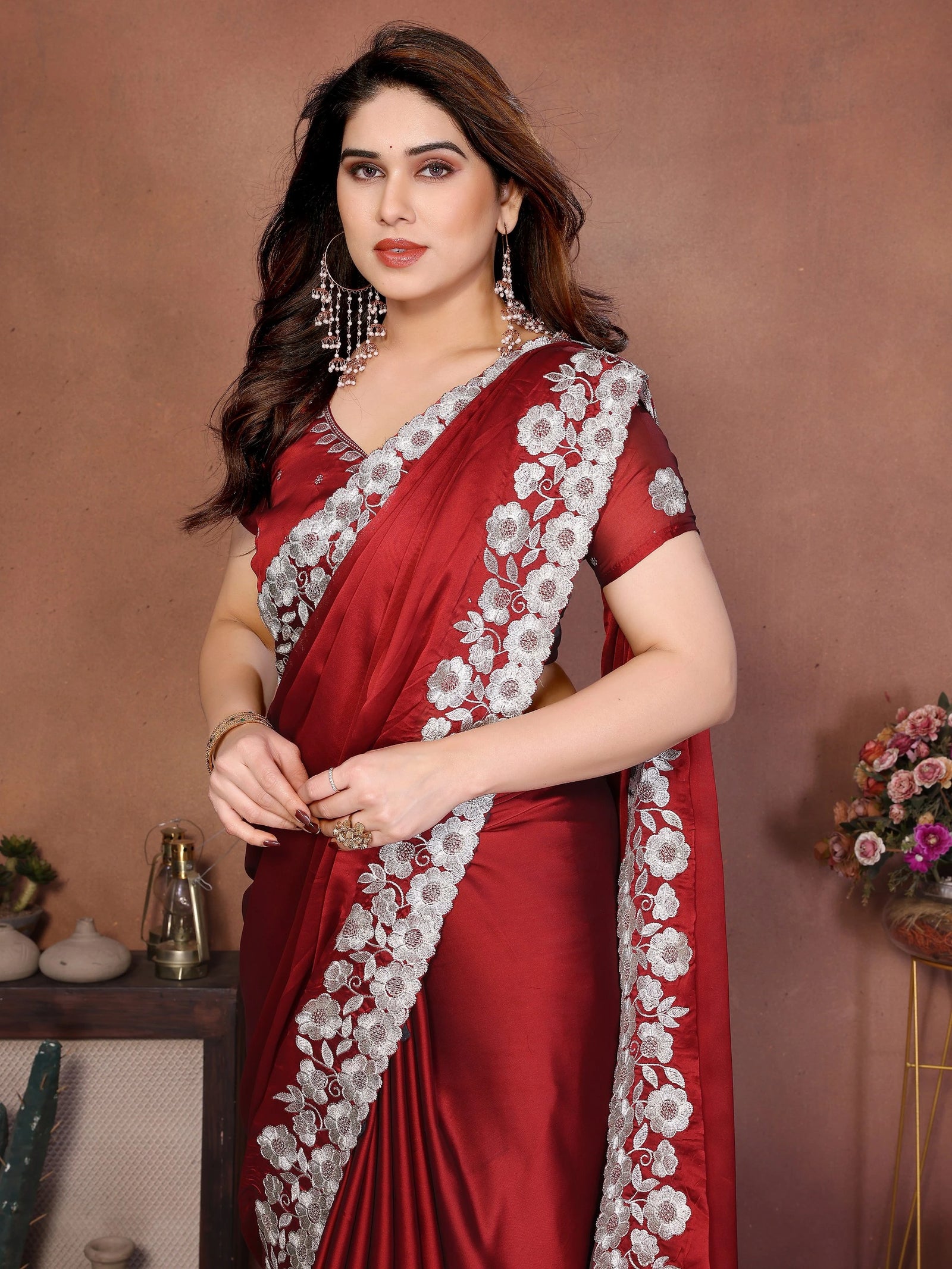 Woman wearing a red saree with white floral patterns against a brown background