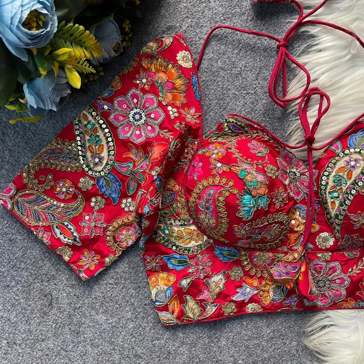 Red embroidered bikini set on a gray surface with flowers in the background