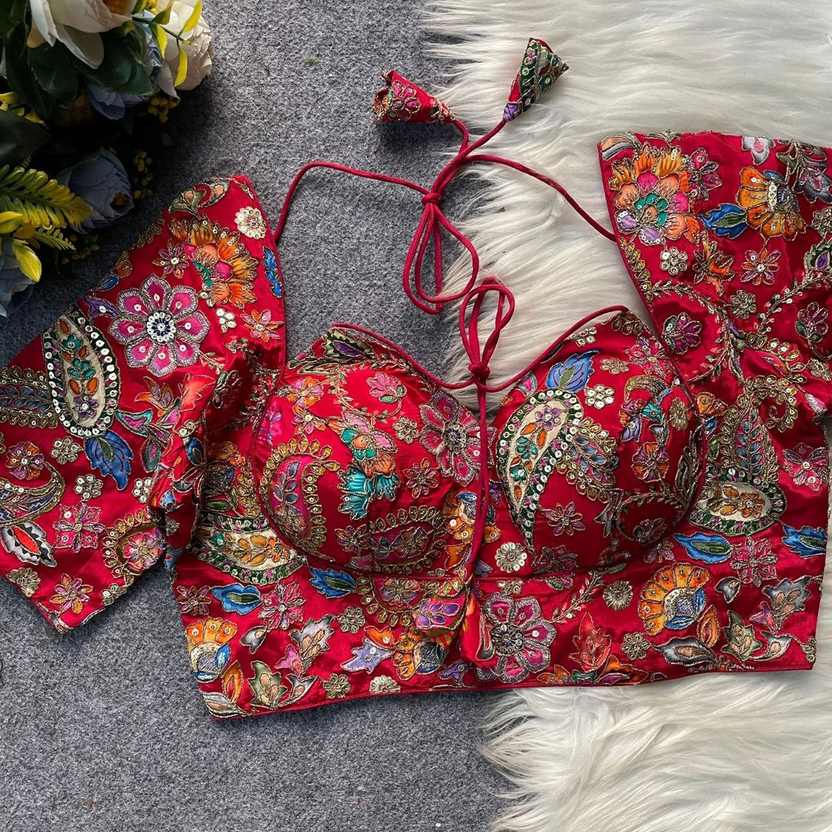 Red embroidered traditional outfit on a textured surface with flowers in the background