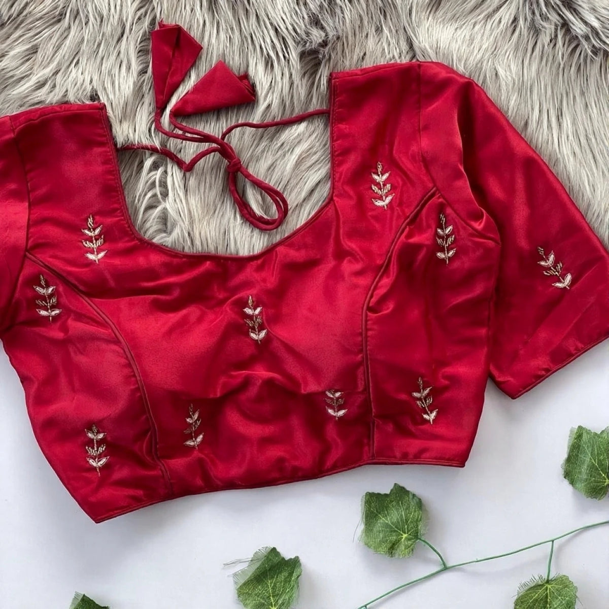 Red embroidered blouse on a textured surface with green leaves.