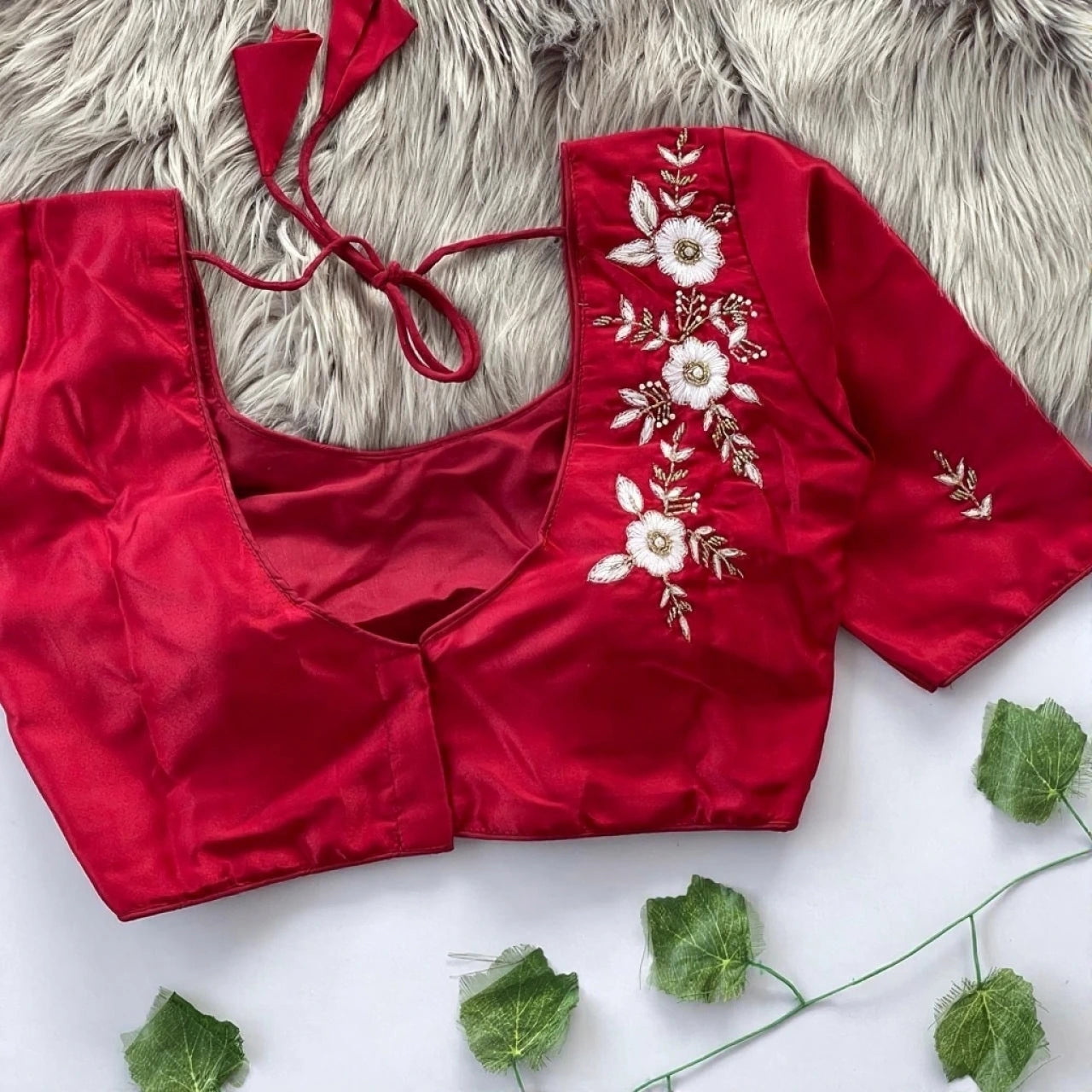 Red blouse with floral embroidery on a textured surface with green leaves.