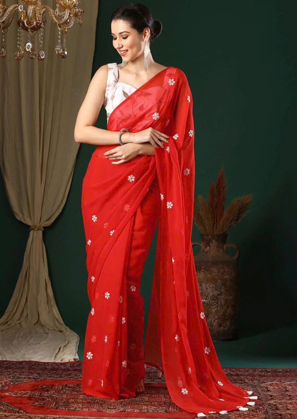 Woman wearing a red saree with white patterns against a green curtain background
