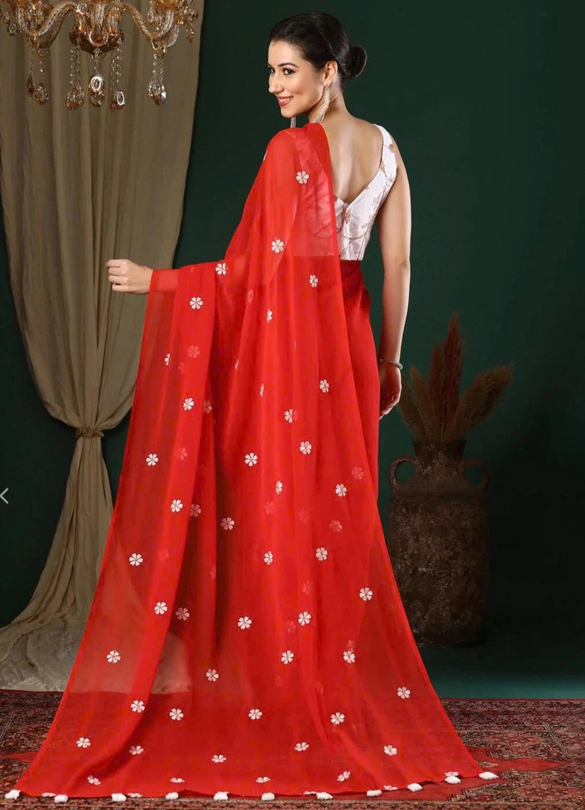 Woman wearing a red saree with white patterns against a dark green background