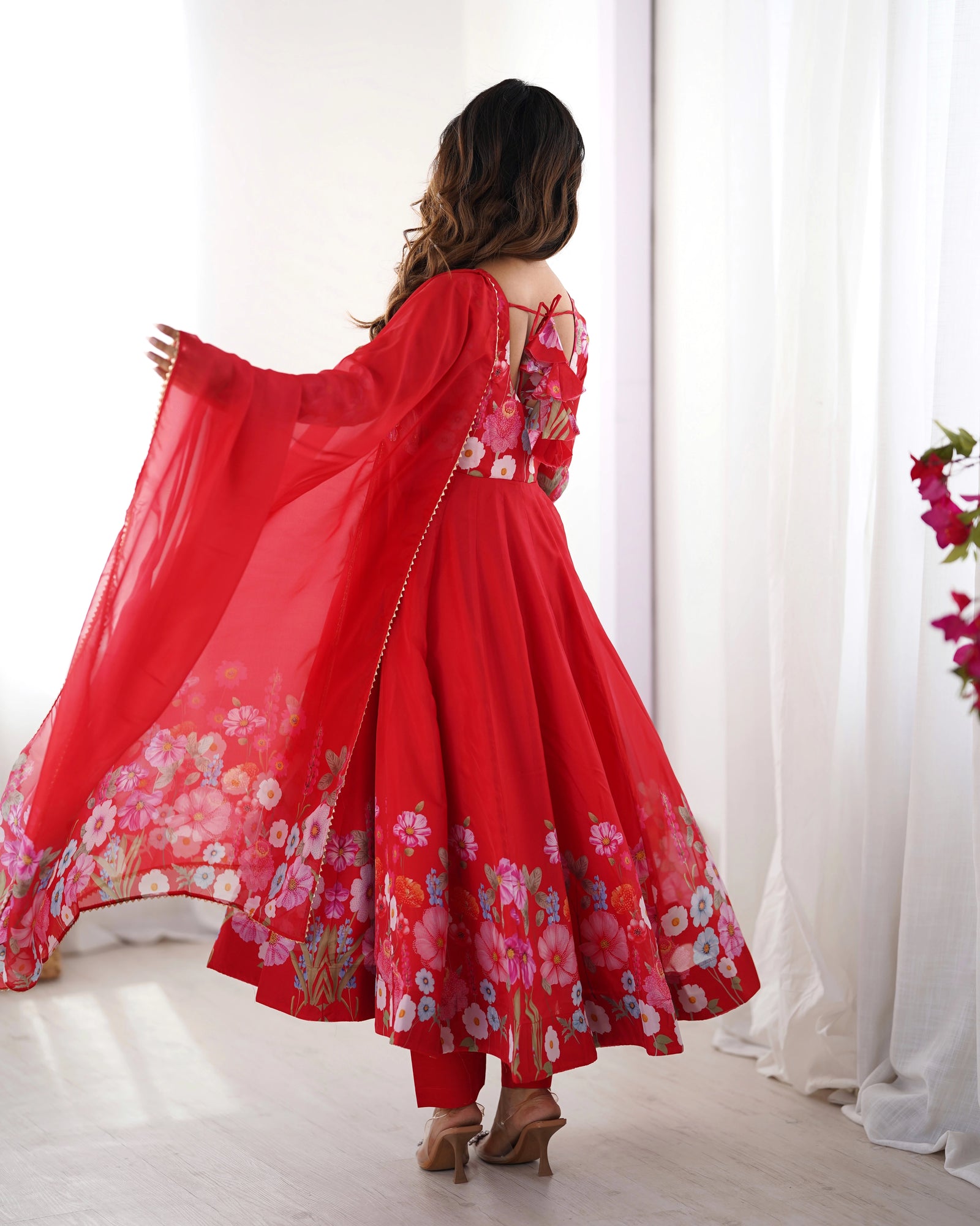 Woman wearing a red floral dress with a sheer dupatta in a bright room.