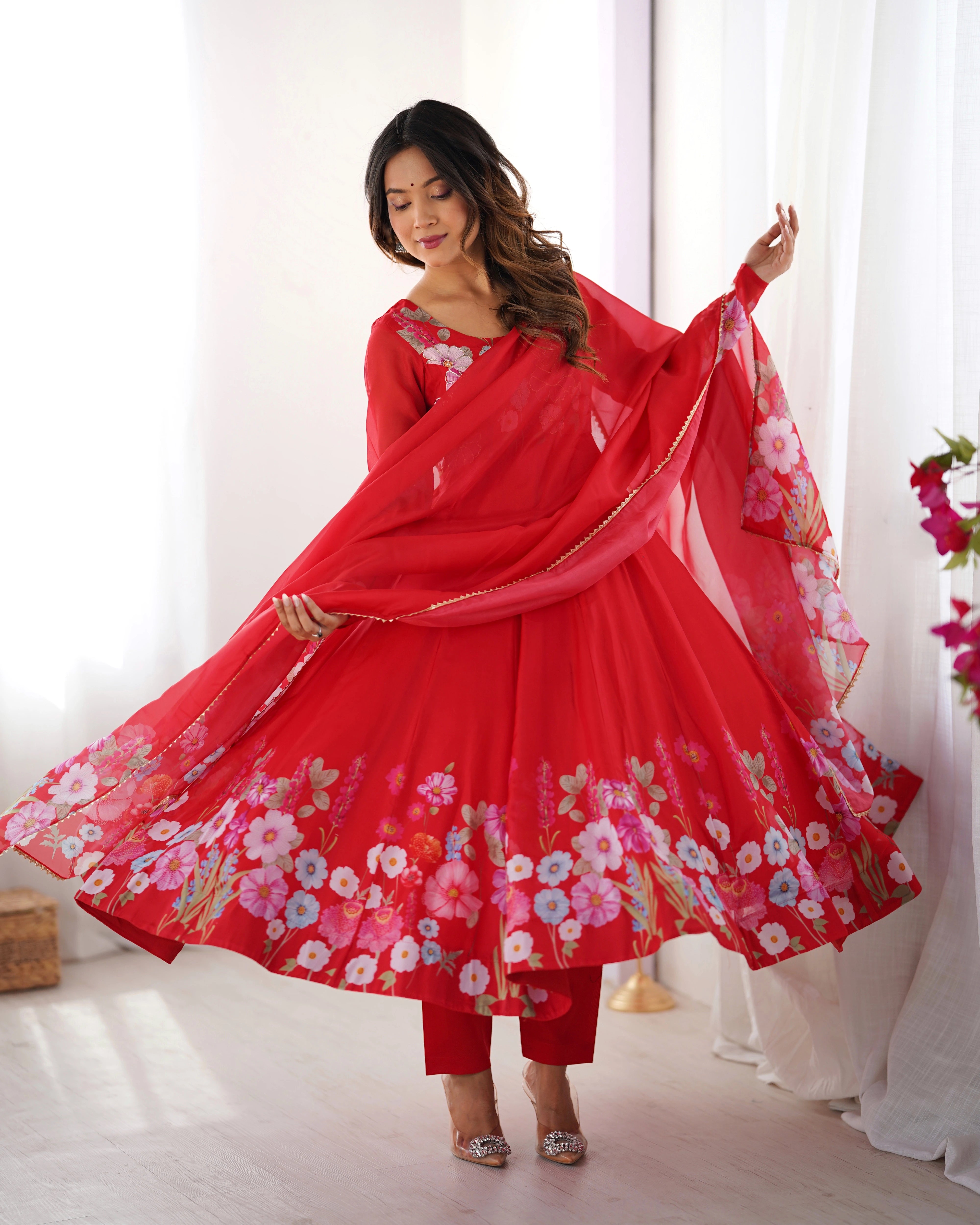 Woman wearing a red traditional outfit with floral patterns in a bright room.