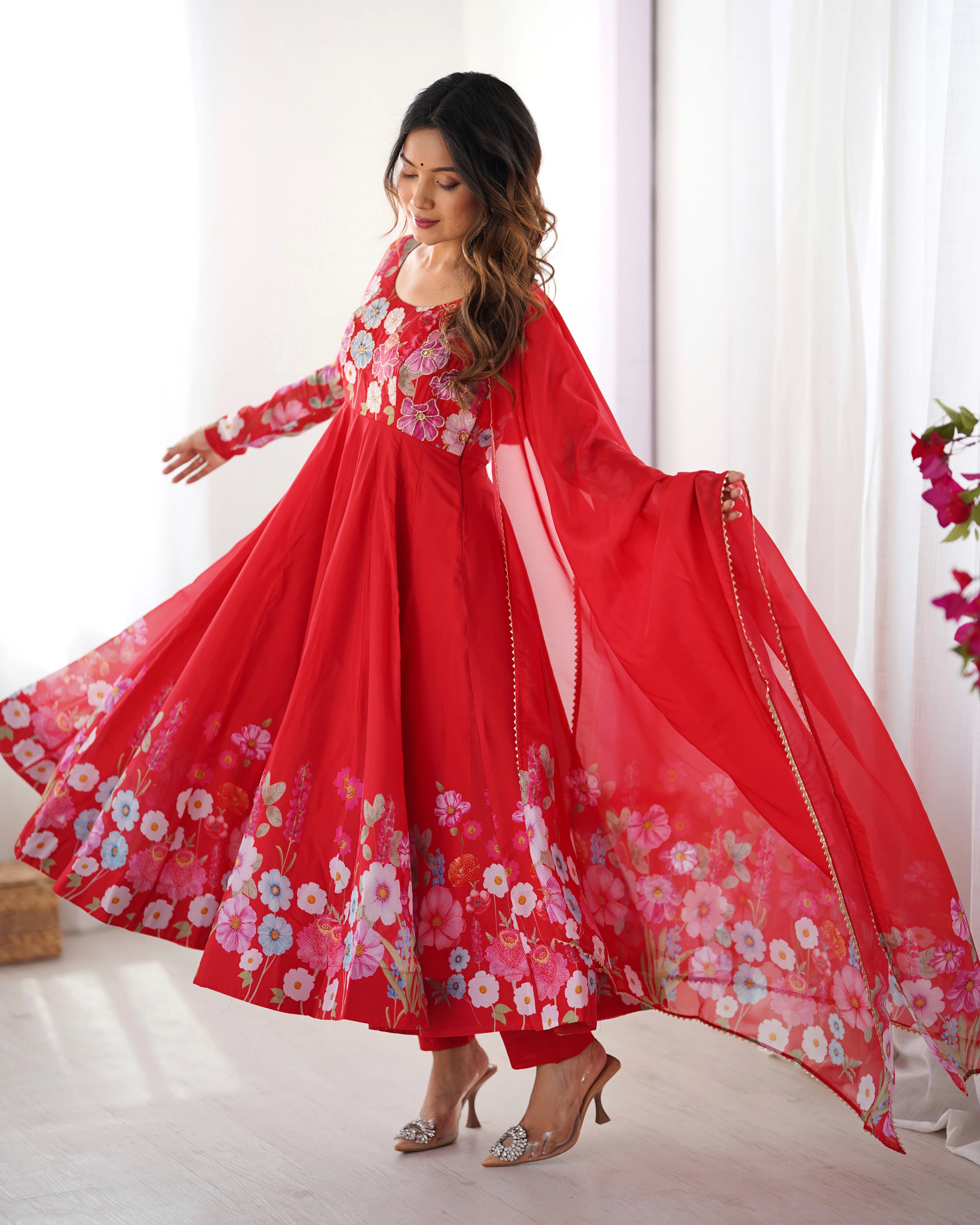 Woman wearing a red floral dress with a flowing skirt in a bright room.