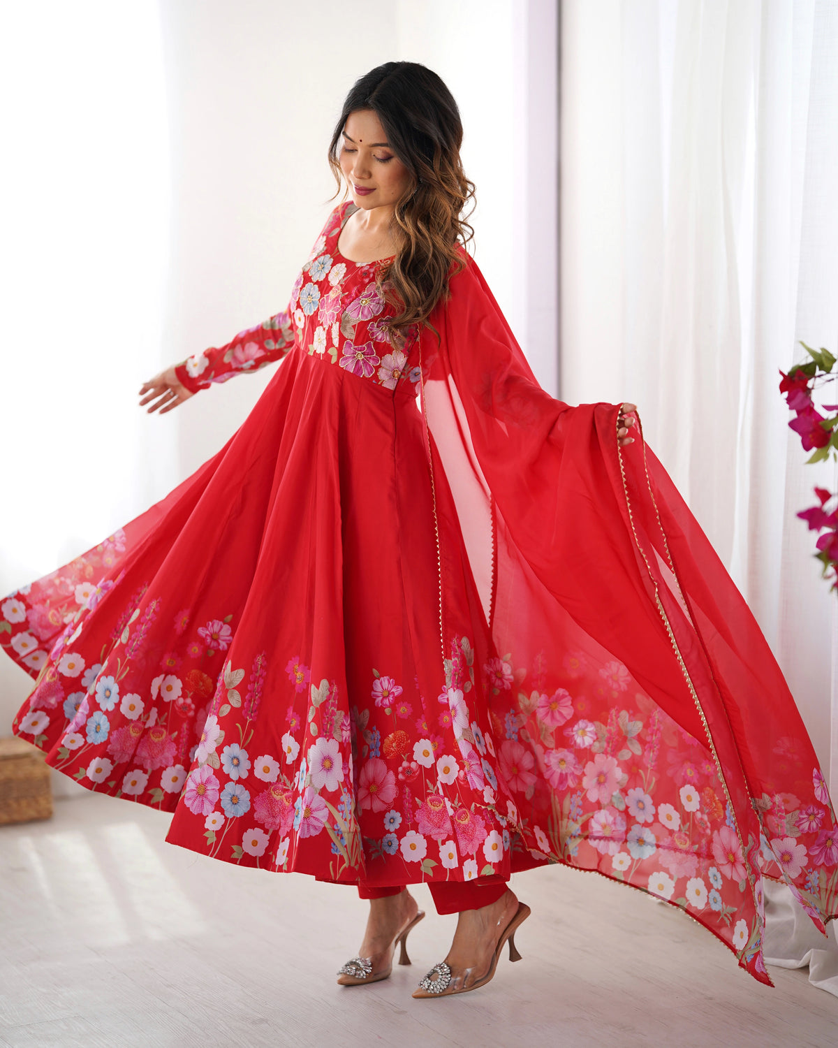Woman wearing a red floral dress with a flowing skirt in a bright room.