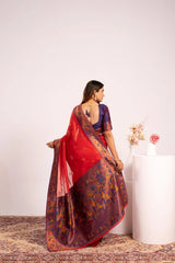 Woman in a red and patterned saree standing next to a white pedestal with flowers on a light background