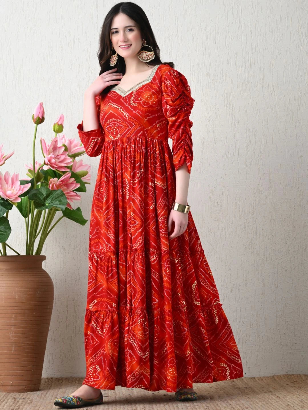 Woman wearing a red patterned dress standing next to a vase with pink flowers on a plain background