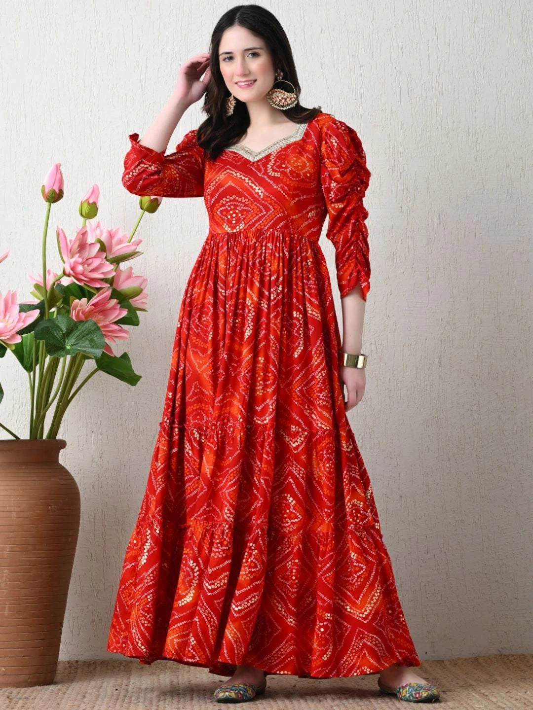 Woman wearing a red patterned dress standing next to pink flowers against a neutral background