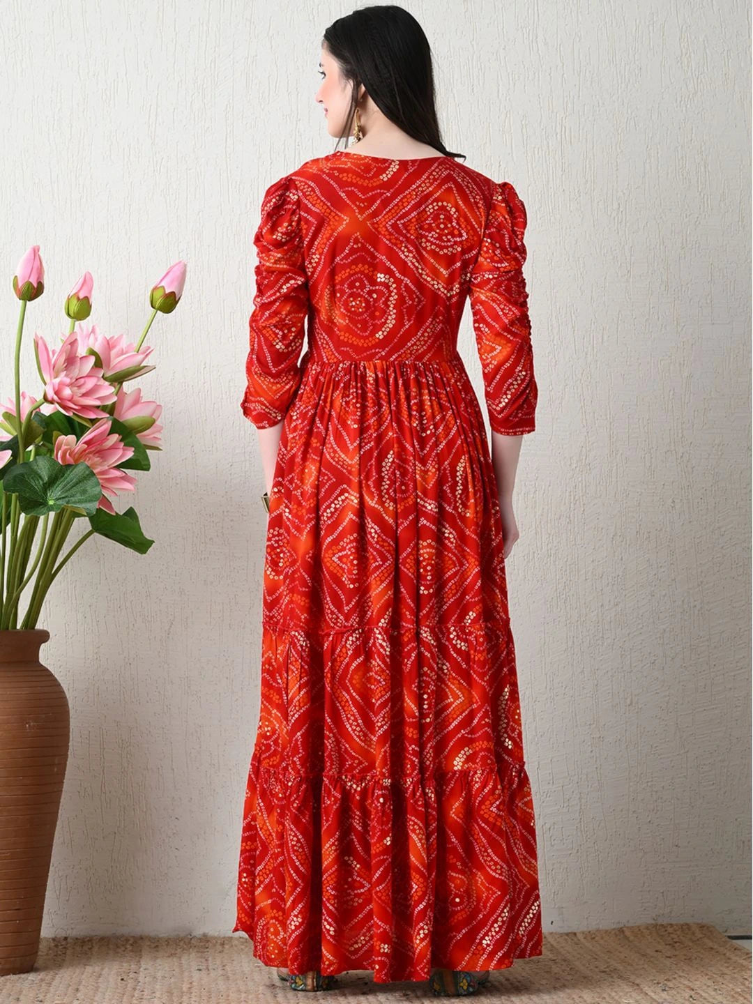 Woman wearing a red patterned dress standing next to a vase with pink flowers on a light background