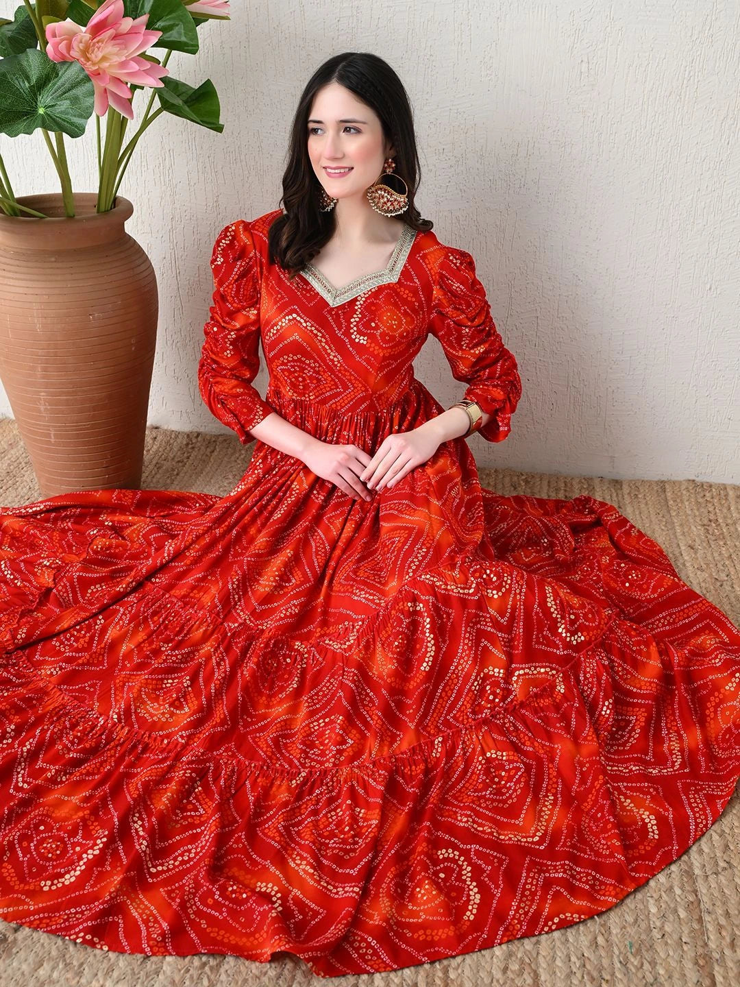 Woman in a red patterned dress sitting on the floor with a plant in the background