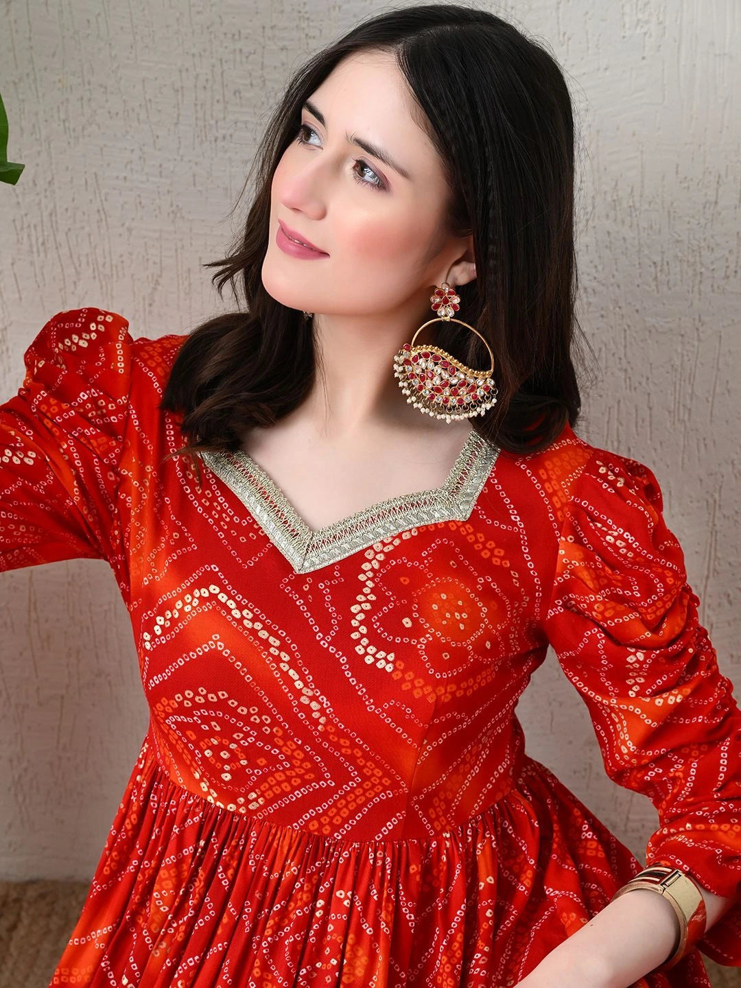 Woman wearing a red patterned dress with gold jewelry against a neutral background