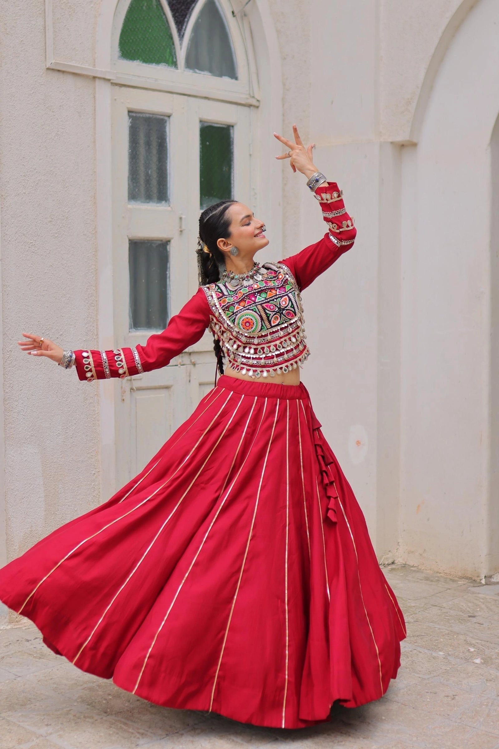Woman in a traditional red and patterned outfit dancing in front of a white building.