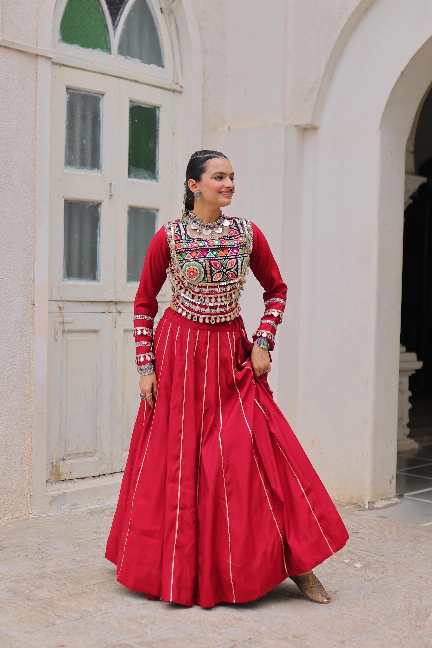 Woman in traditional red outfit with intricate patterns standing in a courtyard.