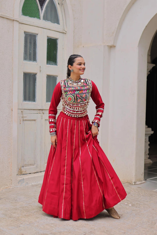 Woman in traditional red outfit with intricate patterns standing in a courtyard.