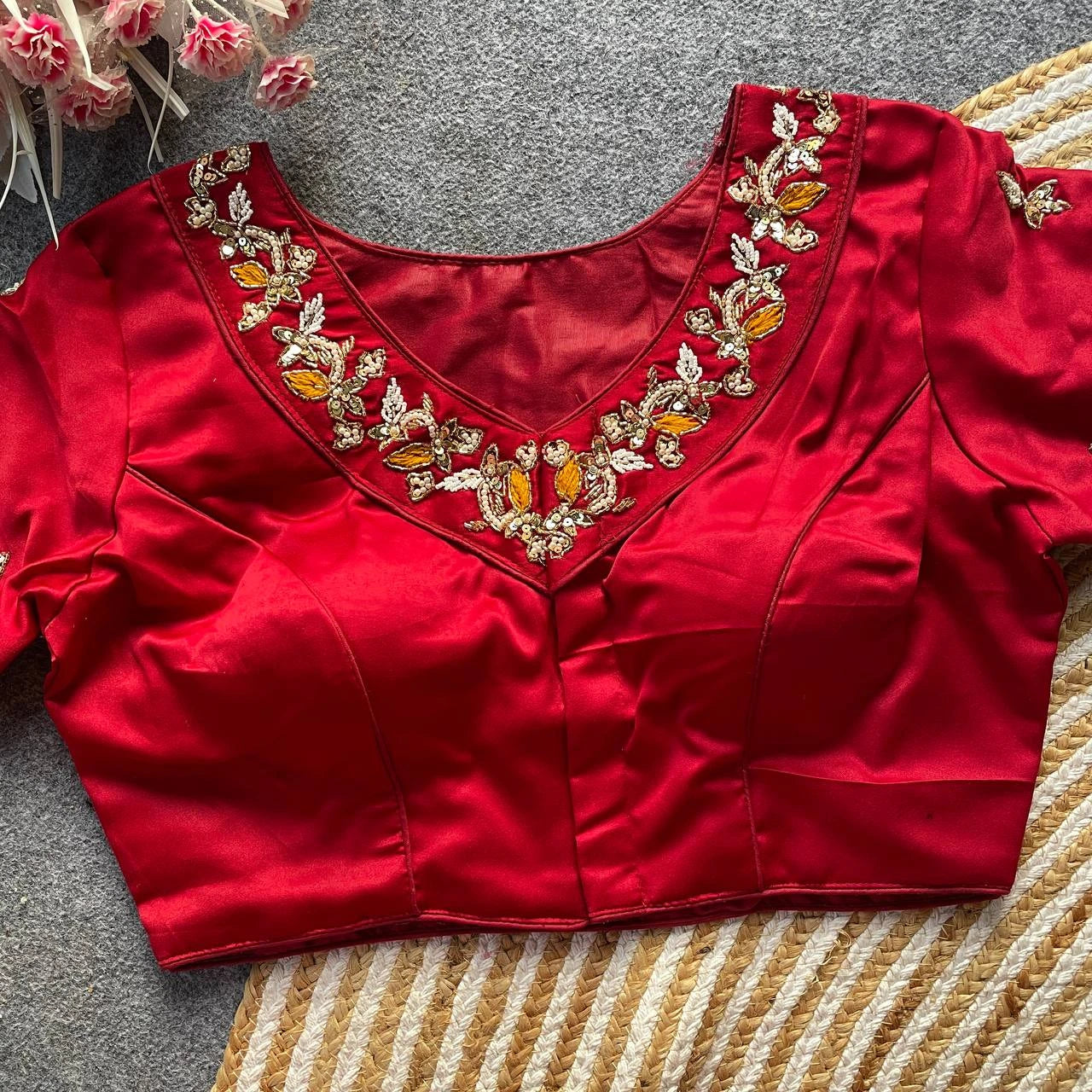 Red blouse with intricate gold and orange embroidery on a textured surface.