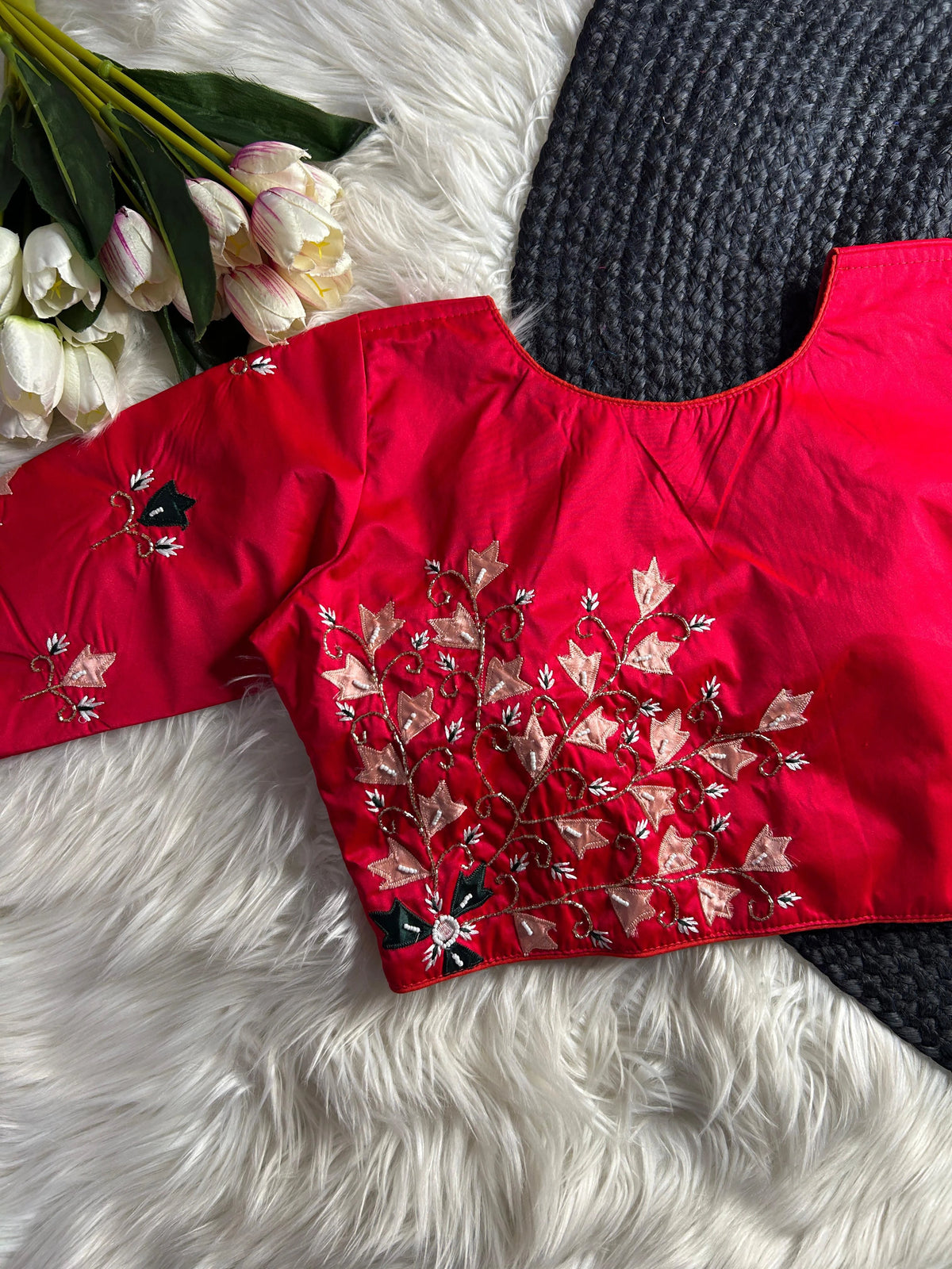 Red embroidered top on a white fur surface with flowers and a black knitted item.