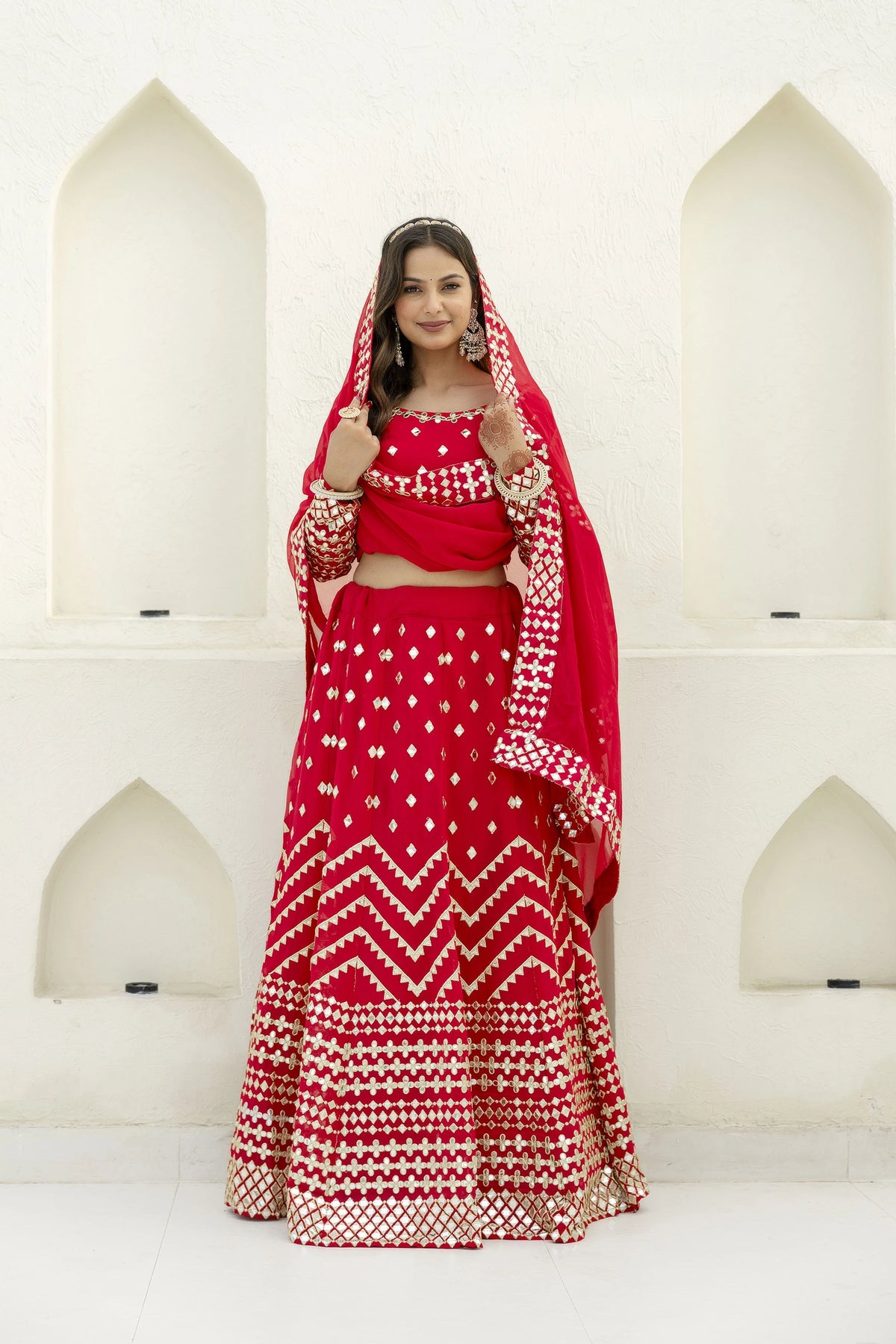 Woman in a red traditional outfit with white patterns standing against a white architectural background