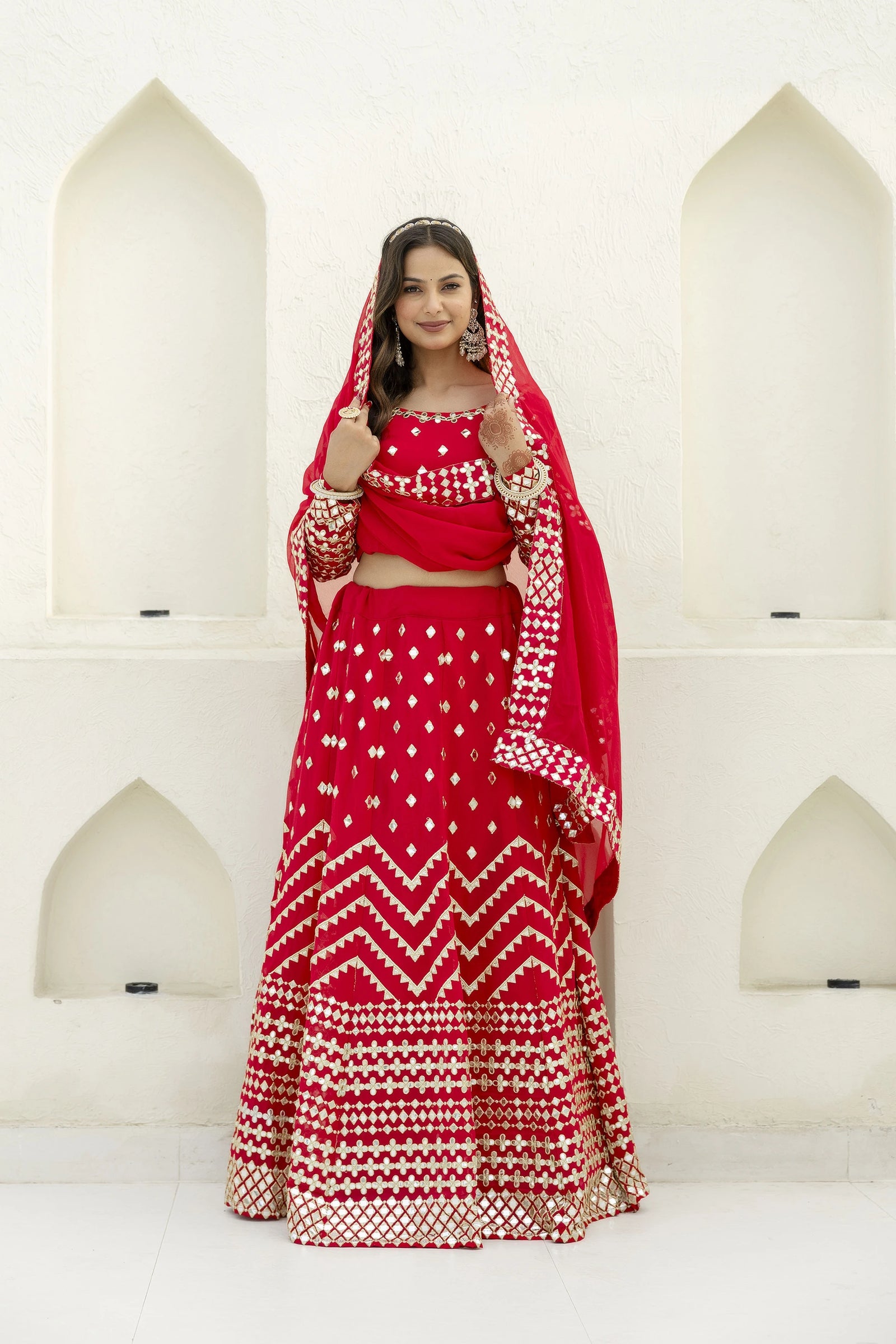 Woman in a red traditional outfit with white patterns standing against a white architectural background