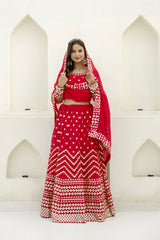 Woman in a red traditional outfit with white patterns standing against a white architectural background