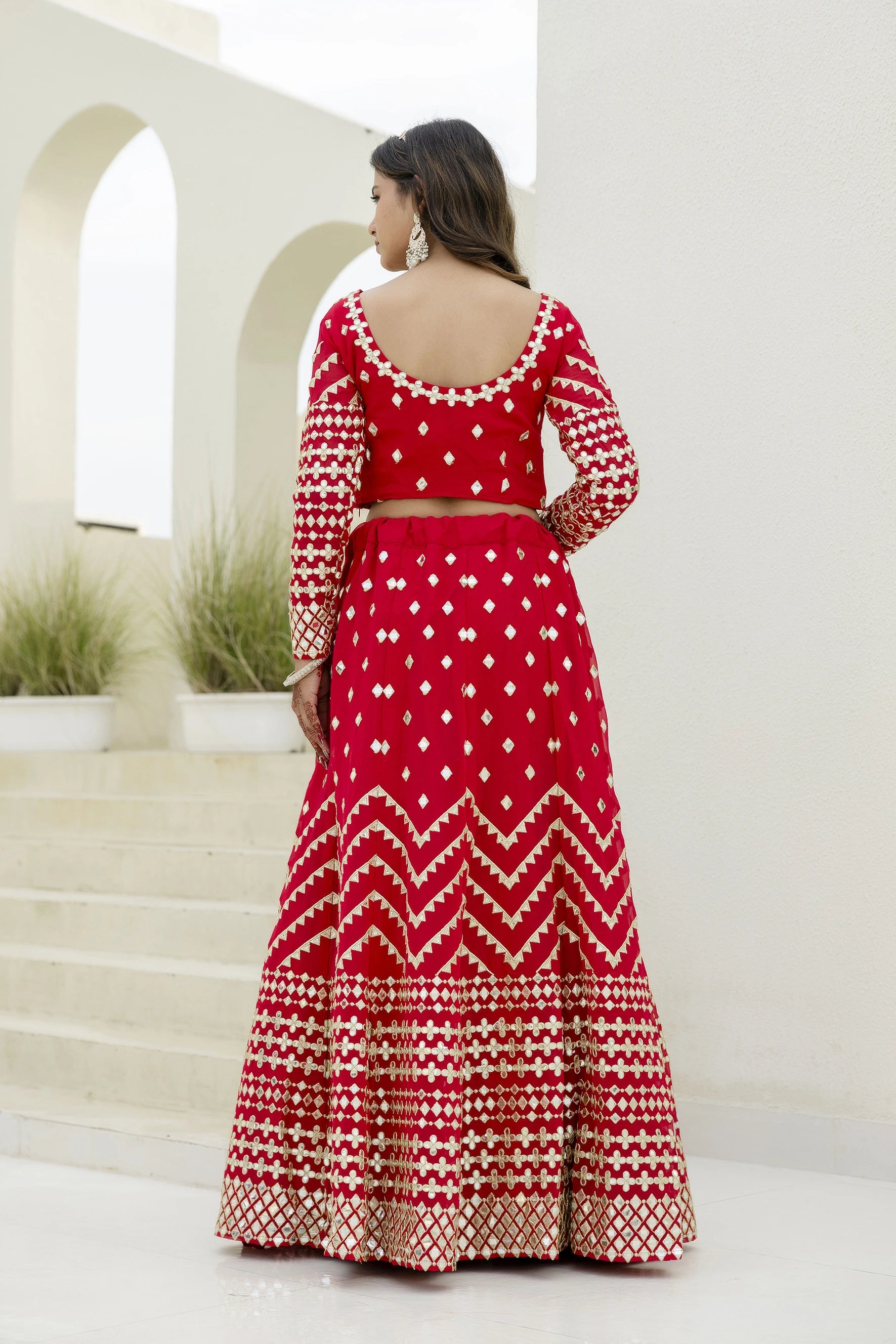 Woman wearing a red and white patterned outfit standing in front of a white architectural background.