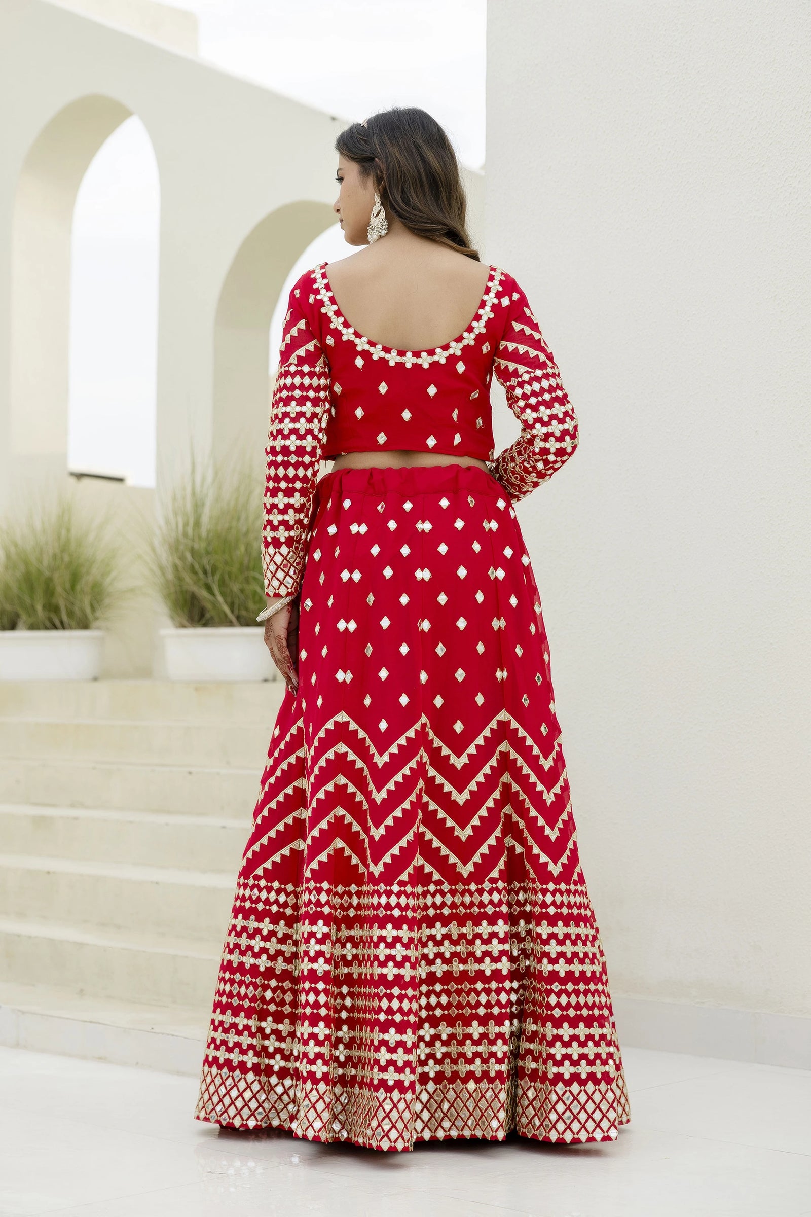 Woman wearing a red and white patterned outfit standing in front of a white architectural background.